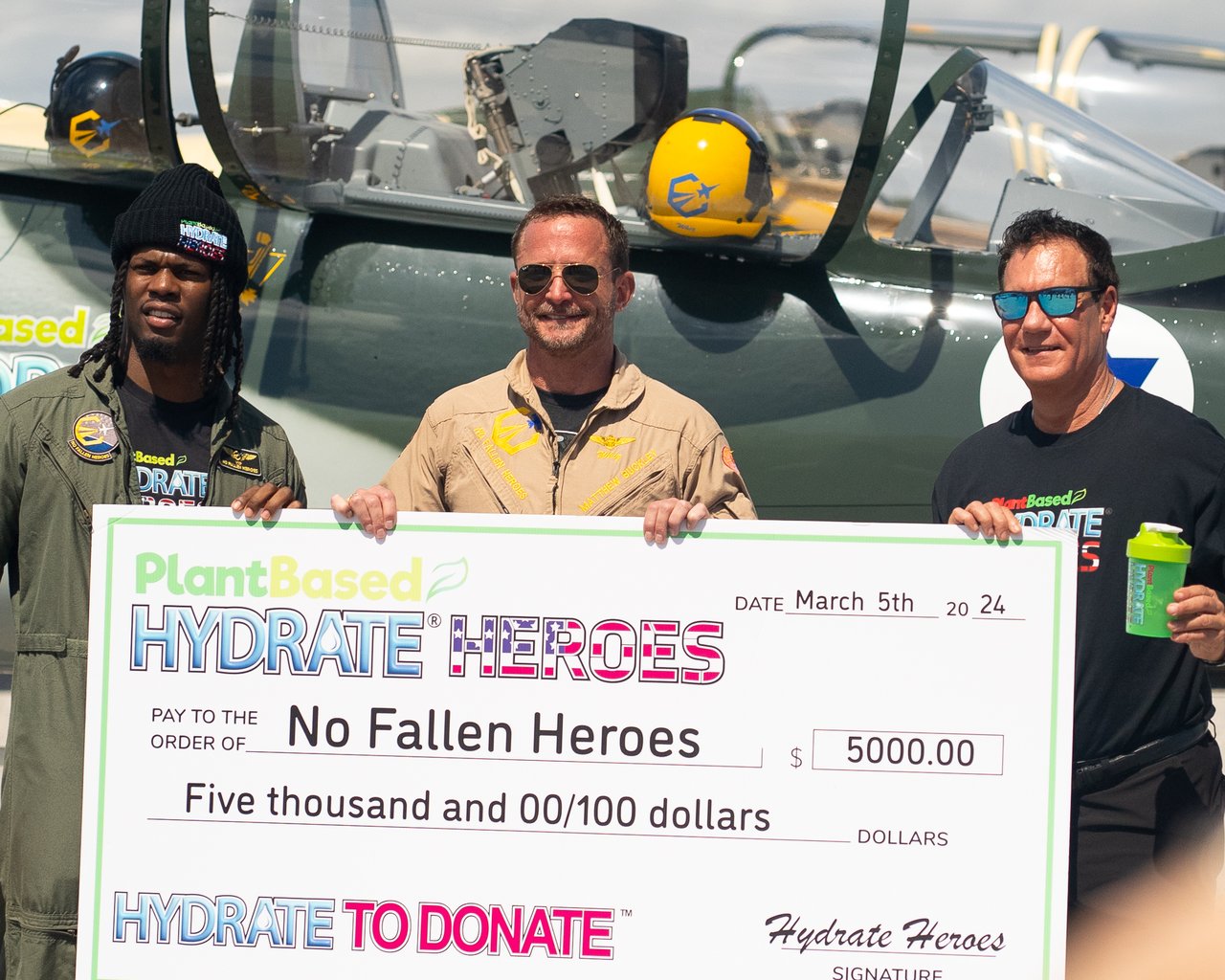 Hydrate To Donate check presentation in front of a warbird aircraft